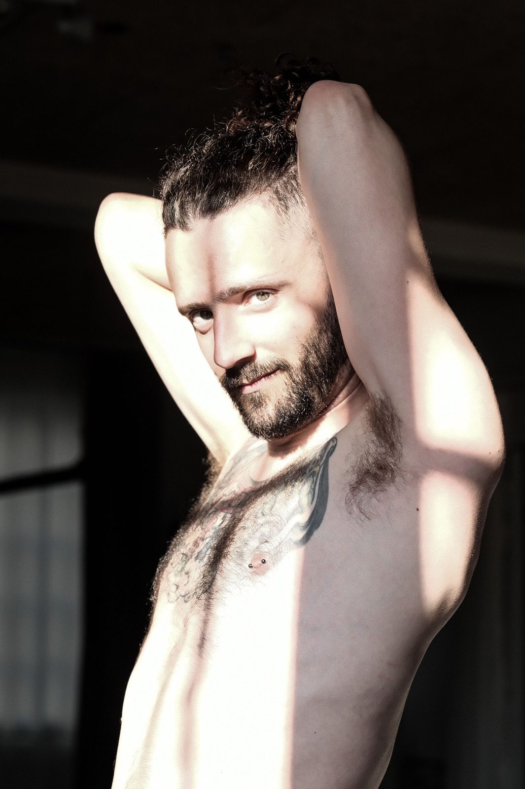 Close portrait of Princess Boy, shirtless with both arms raised, in warm side light